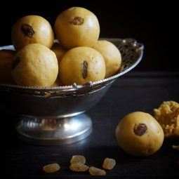 Golden besan ladoos topped with raisins on a silver serving dish