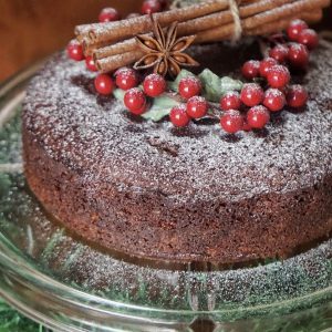 Christmas fruit cake dusted with icing sugar and decorated with cinnamon sticks, star anise and red berries on a glass cake stand.