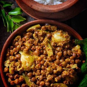 Black chickpeas, ivy gourd and hog plums in coarse coconut masala in a clay bowl, with rice behind it.