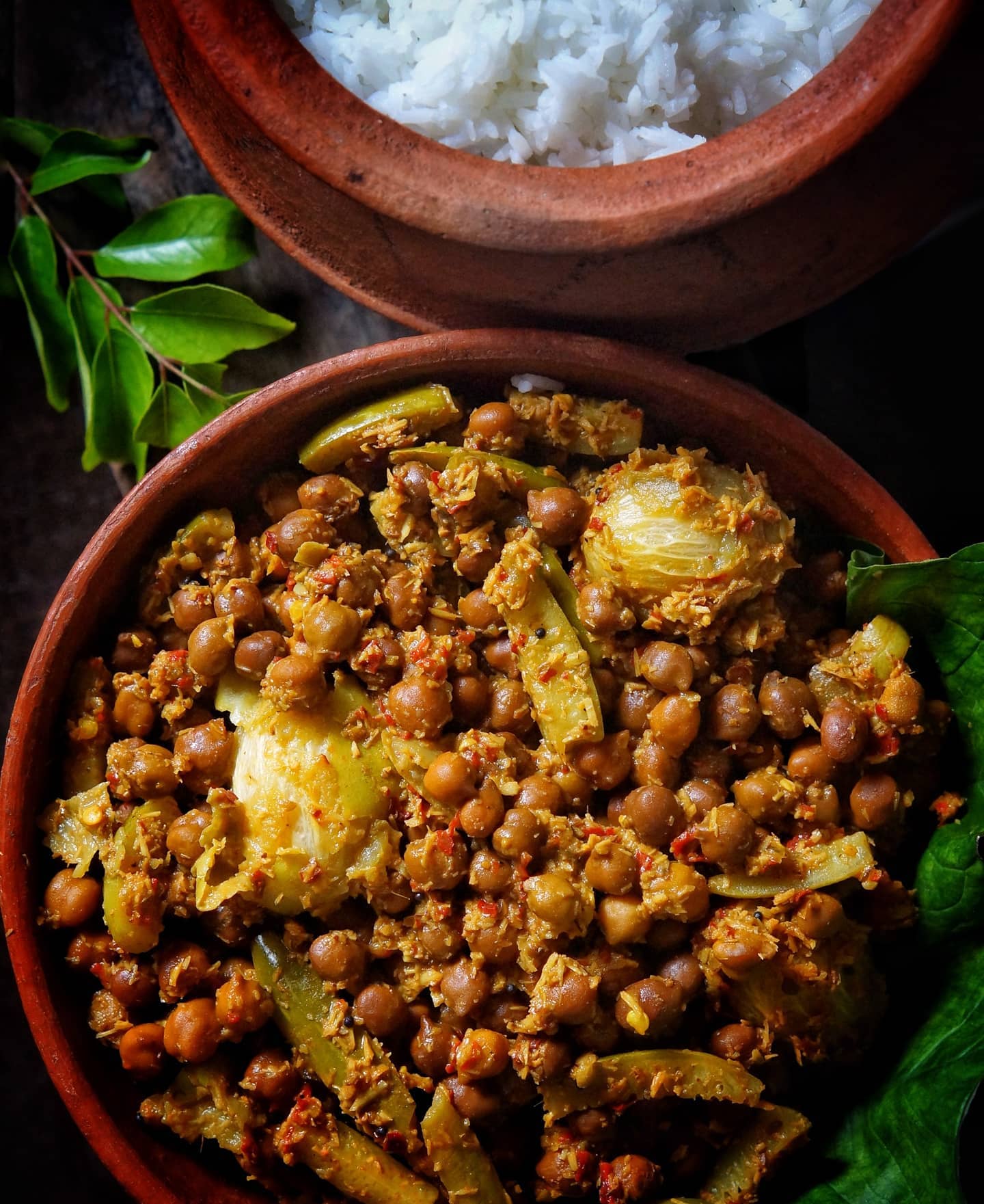 Black chickpeas, ivy gourd and hog plums in coarse coconut masala in a clay bowl, with rice behind it.