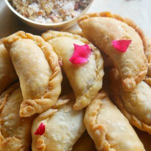 Golden crimped Karanji pastries with rose petals and coconut filling alongside