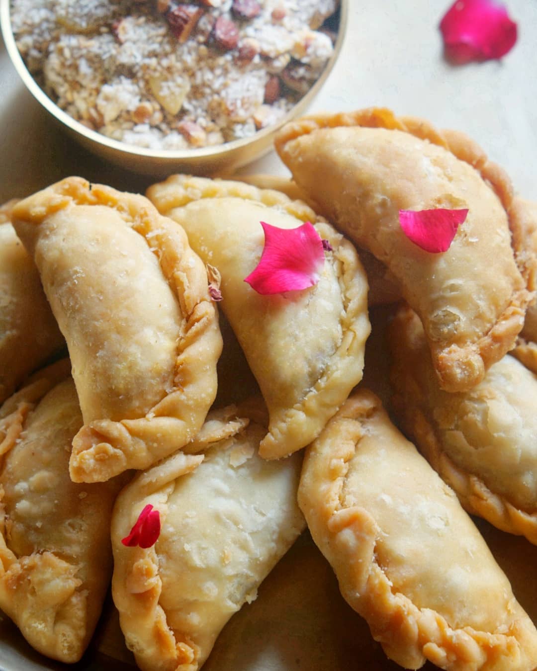 Golden crimped Karanji pastries with rose petals and coconut filling alongside