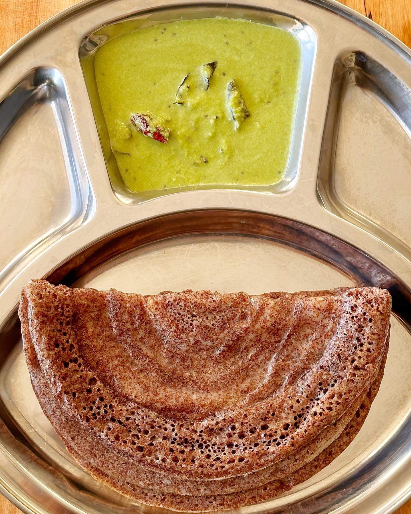 Ragi dose served with green kothambari chutney on a stainless steel plate
