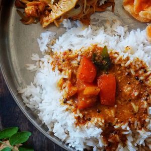 Temple-style tomato Saar poured over white rice on a steel meal plate