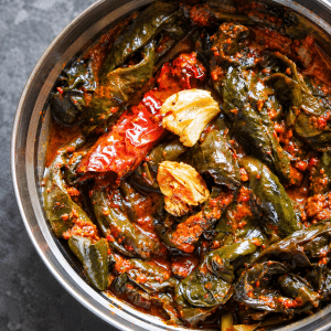 Cooked colocasia leaf knots in red Pulimunchi masala, topped with browned garlic and a dried red chilli in a steel bowl.